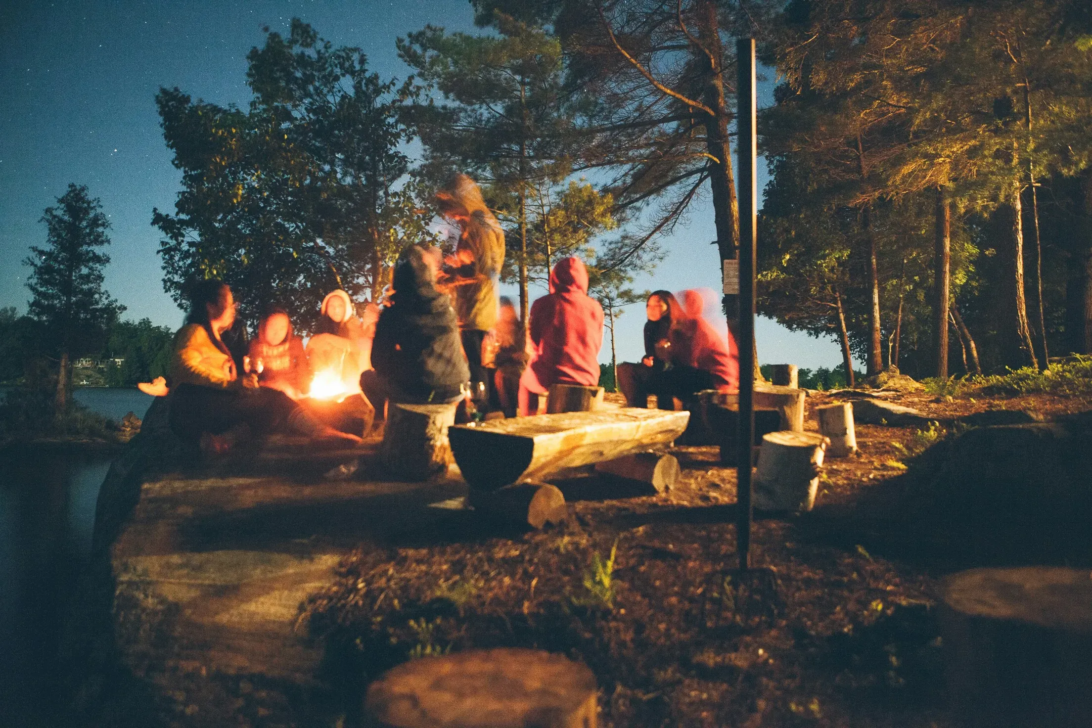 Evening campfire scene with people roasting marshmallows under the stars.