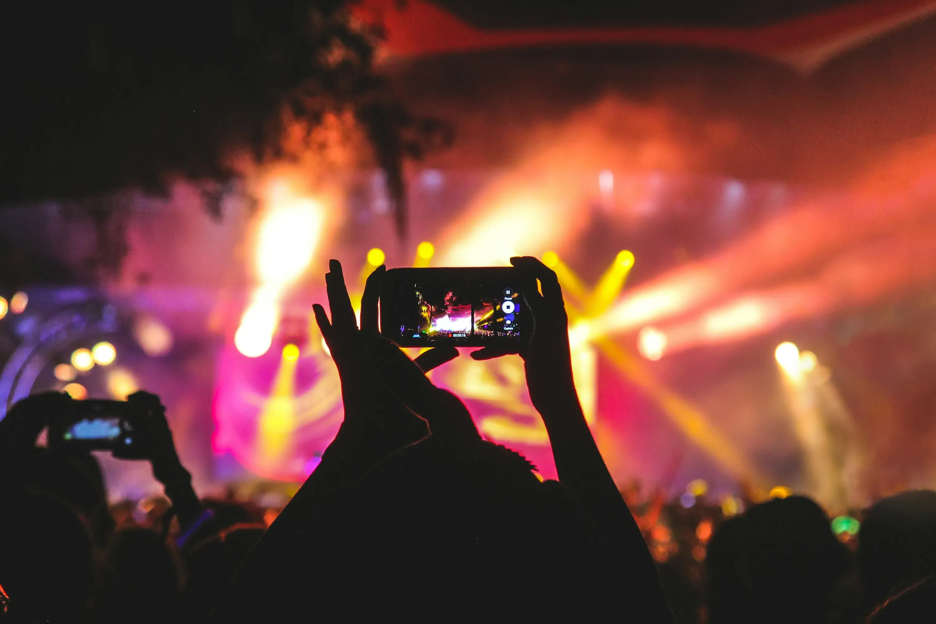Outdoor music festival crowd with stage and lights at sunset.