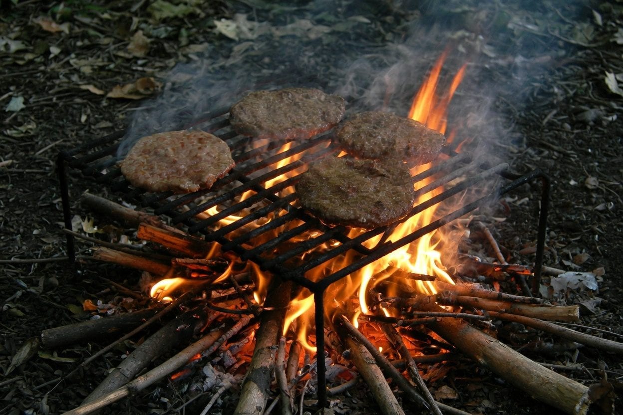 Grilled meat skewers on a charcoal BBQ grill with flames and smoke