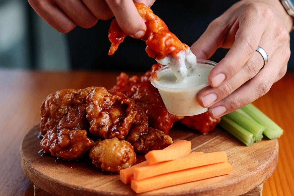 Close-up of wings being dipped into sauce