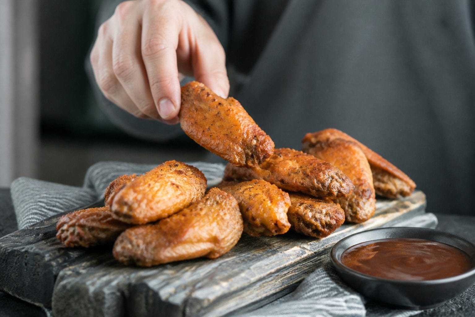Crispy wings on a wooden board beside sauce