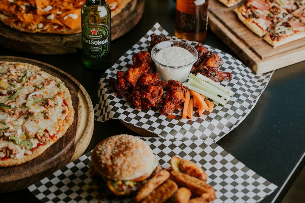 Pub table spread with wings, pizza, burgers, and beer