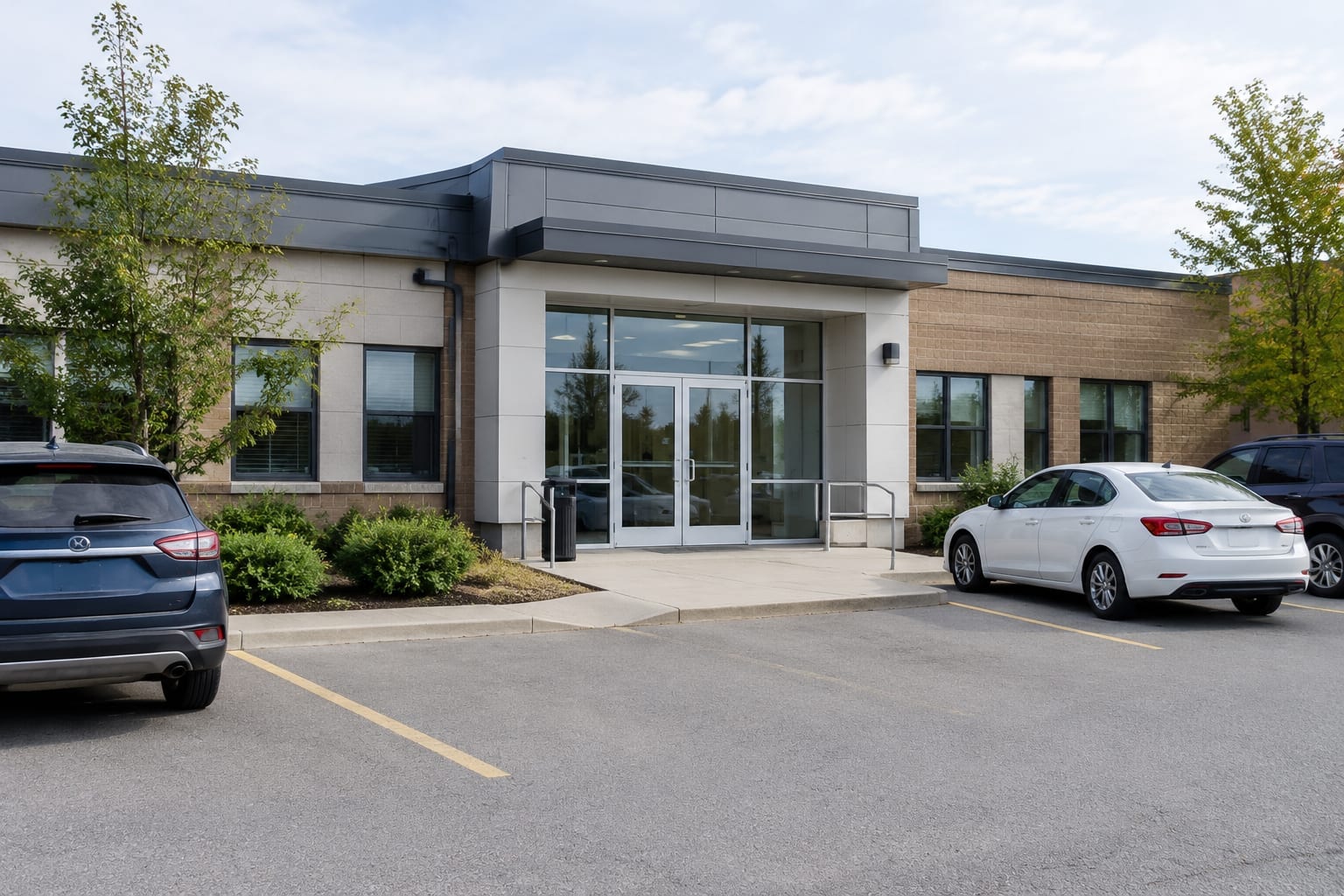 The entrance of a low-rise police station building in Ottawa with a few cars in the parking lot