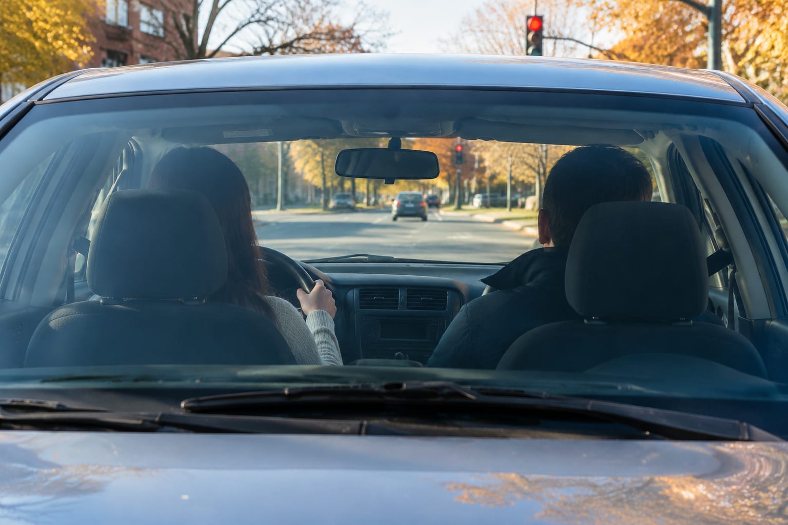 A student driver and an instructor in a dual-control car at an Ottawa intersection on an autumn morning