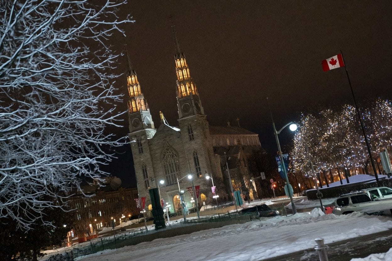 The Rink of Dreams at Ottawa City Hall glowing with LED lights at night, skaters gliding across the illuminated ice surface