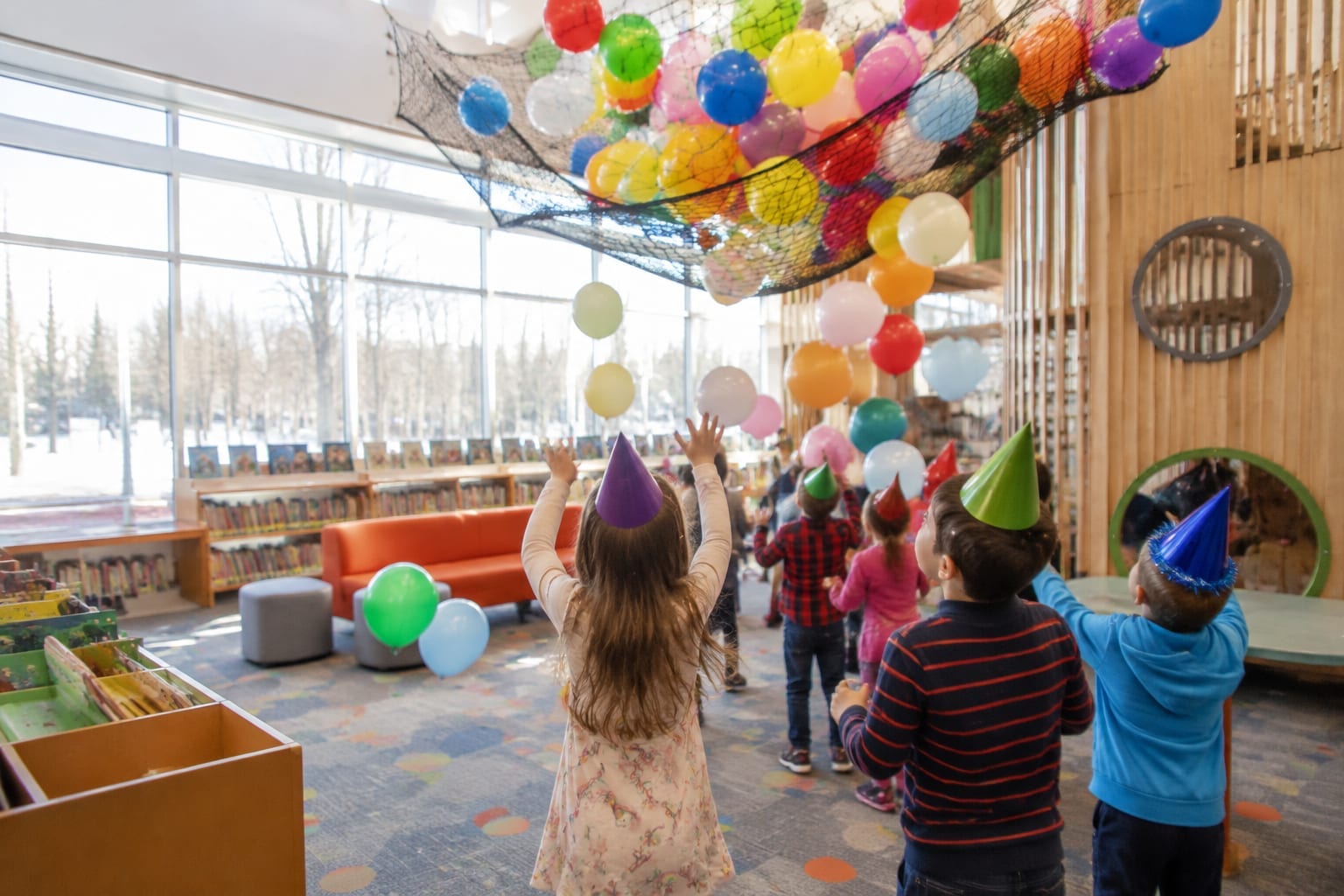 Young children in party hats cheering as balloons fall at a library countdown