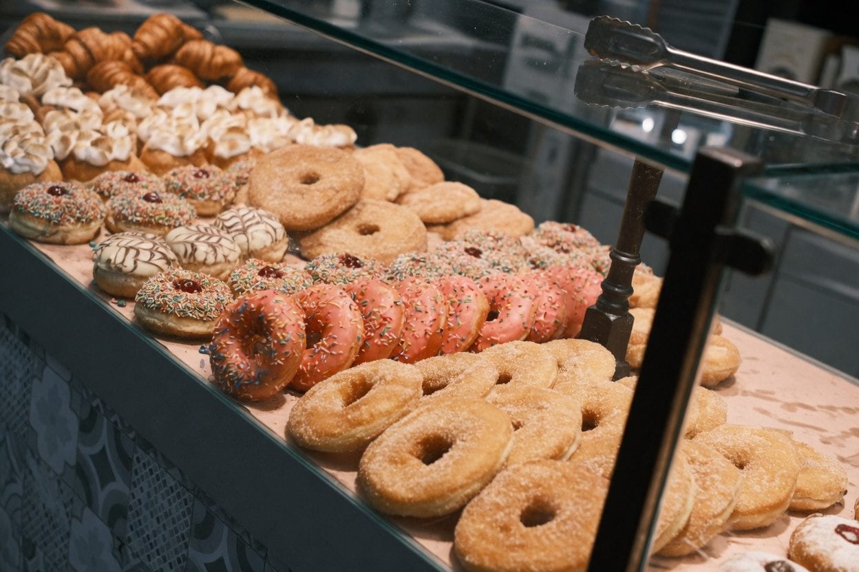 Assorted donuts in a glass display case with colourful glazes and toppings