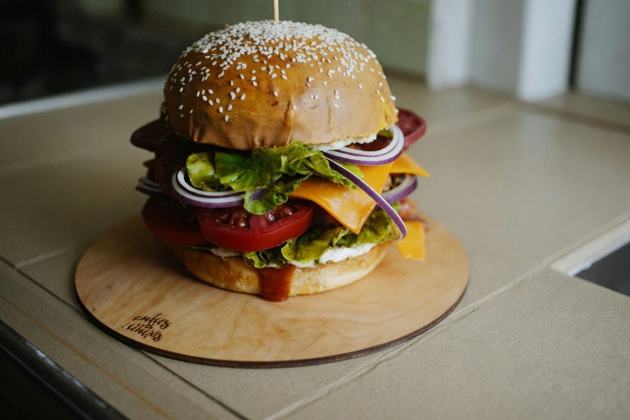 Gourmet burger with toppings on wooden cutting board